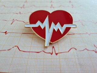 Cardiogram chart with small red heart on table closeup