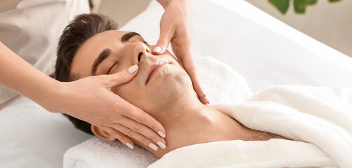 Fototapeta na wymiar Handsome man having face massage in spa salon