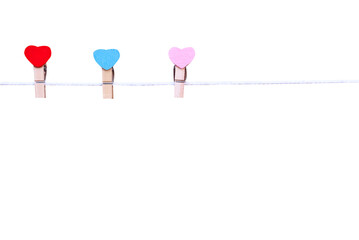 Three wood clothes pins in heart shape patterns hanging on white rope isolated on white background...