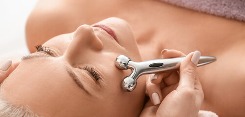Obraz na płótnie Canvas Mature woman receiving face massage in beauty salon, closeup