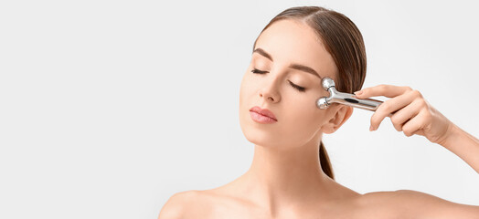 Fototapeta premium Beautiful woman with facial massage tool on white background