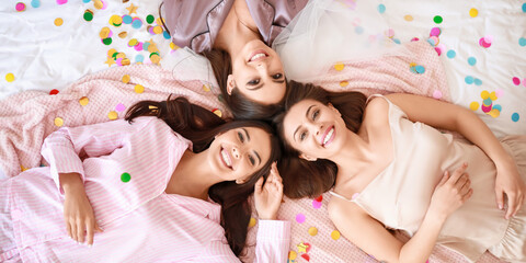 Beautiful young women at hen party lying on bed, top view