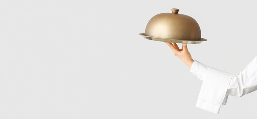 Hand of waiter holding tray and cloche on light background with space for text