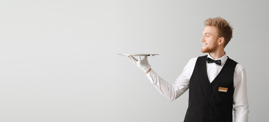 Handsome waiter with empty tray on light background with space for text