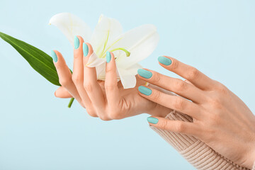 Hands of woman with beautiful mint manicure holding flower on light blue background, closeup