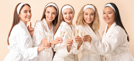 Beautiful young women in bathrobes drinking champagne on light color background