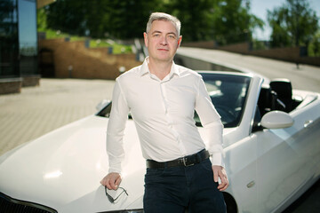 Attractive respectable man with glasses is leaning on his cabriolet