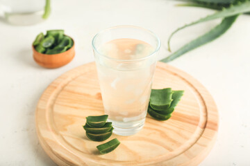 Board with glass of aloe juice and leaves on white background