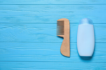 Baby hair comb and shampoo on color wooden background