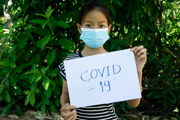 Girl wearing mask stand and holding paper with wording COVID-19 with green background.