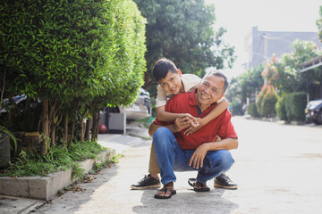 Asian school boy on a piggy back ride with his grandfather, smiling and looking to the camera....
