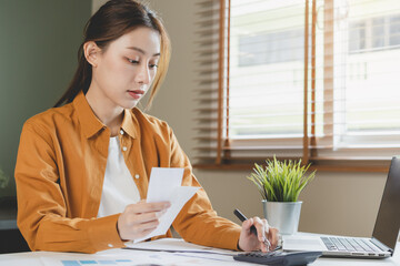 Asian young employee, business woman calculate tax income and expenses, bills, credit card for payment or payday on table at home office. Financial, finance people concept.