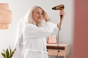 Morning of mature woman with hair dryer in bathroom