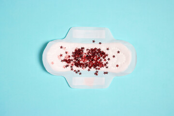 Menstrual pad with red glitter stars on blue background © WindyNight
