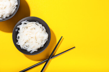 Bowls with tasty noodles and chopsticks on yellow background