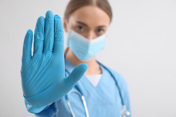 Fototapeta Female nurse showing STOP gesture on light background obraz