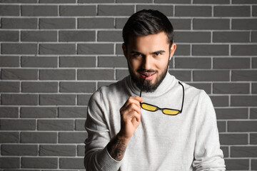 Bearded man holding sunglasses near grey brick wall