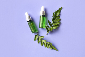 Bottles of natural serum and fern leaves on lilac background