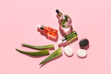Composition with bottles of natural serum, spa stones and aloe leaves on pink background
