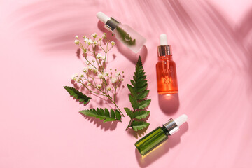 Bottles of natural serum, fern leaves and gypsophila flowers on pink background