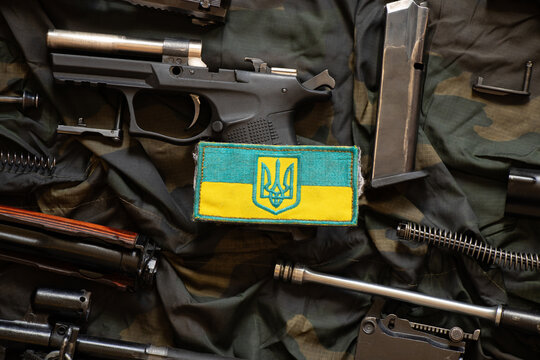The patch of the flag of Ukraine lies on a disassembled machine gun on a green camouflage fabric, war in Ukraine