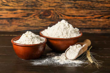 Scoop and bowls with wheat flour on dark wooden background