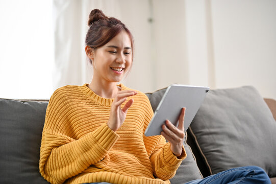 Beautiful Young Asian Woman Sitting On Comfortable Sofa And Using Portable Tablet