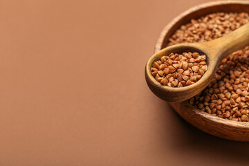 Bowl and spoon with buckwheat grains on color background, closeup