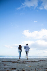 Young couple from behind is running at the beach to the sea in Larnaca, Cyprus