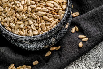 Bowl with peeled sunflower seeds and napkin on grunge background, closeup