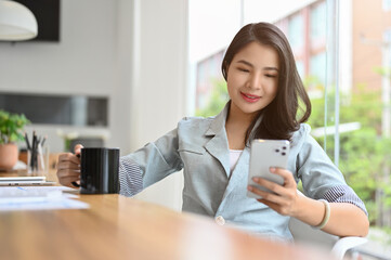 Asian businesswoman sipping coffee while using a smartphone in the team meeting.