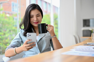 Gorgeous Asian businesswoman sipping coffee and reading a business news on her phone