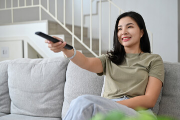 Beautiful young asian woman sits on couch enjoy watching TV show in the living room.