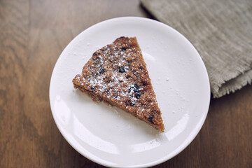 Part of the pie is on a white plate on the table. A piece of lemongrass with blueberries and cranberries without milk and eggs on flaxseed flour. The concept of healthy eating
