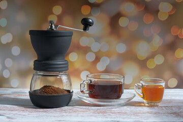 coffee cup, manual coffee grinder, and honey on the table with a bokeh background
