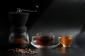coffee cup, grinder, and coffee beans with honey on a black background, light shines through.

