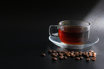 cup of coffee and coffee beans on black background with light passing through
