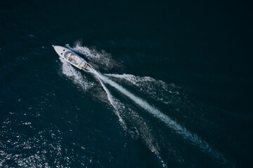 Modern big white boat with people moving fast on dark water top view. White yachts in the sea.