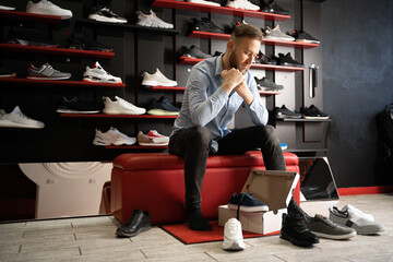 Cheerful man chooses shoes in a sports shop while sitting in fitting room of modern store