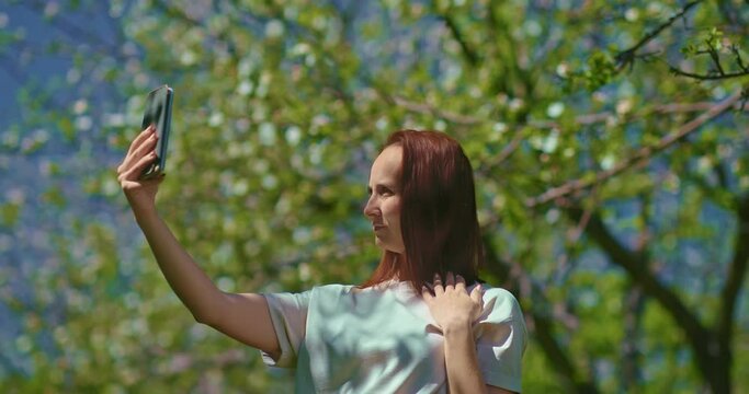 joyful woman is taking selfie by mobile phone in blooming garden, 4K, Prores