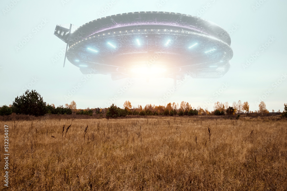 Wall mural ufo, an alien saucer hovering above the field in the clouds, hovering motionless in the sky. unident