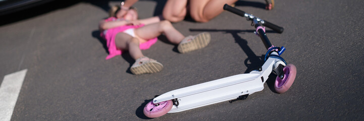 Little girl lying on the asphalt with scooter and her mother after collision with car © H_Ko