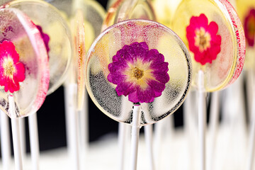 Beautiful lollipop caramel with edible flowers over on dark background. - 512256010