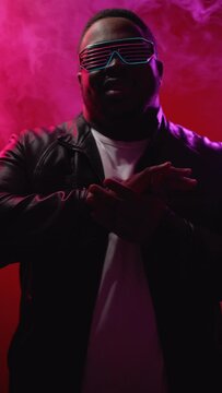 Rap performance. 90s party. Nightclub event. Cool stylish confident man in futuristic sunglasses singing hip hop song on neon light stage vertical.