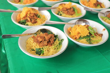 
Mie Ayam, noodles with chicken pieces, vegetables in a white bowl on a green table. Usually served with meat ball, chili sauce, and salty crispy crackers.
