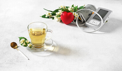 a cup of tea with jusmine flower and blood pressure monitor, beverage against heart pressure, selective focus, copy space in the right corner