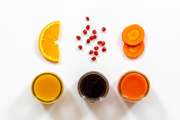 three kinds of juices orange, pomegranate, carrot on a white surface, carrot and orange slices, pomegranate seeds, top view, healthy food concept, vitamin detox, diet