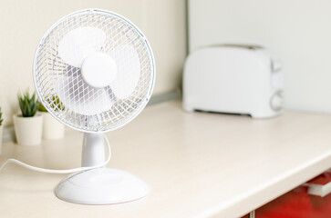 A small fan on the kitchen table. The concept of cooling and ventilation of the house.