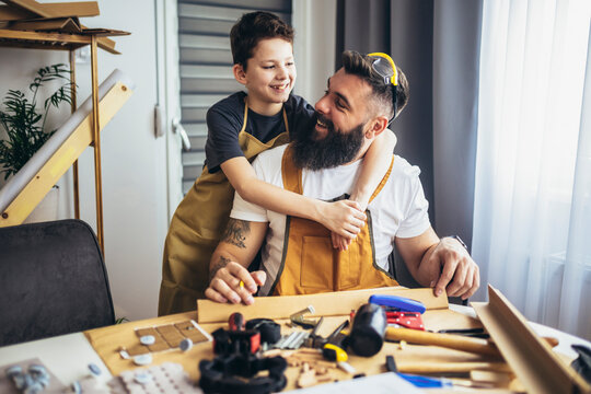 Father teaches his son to plan wood in a carpentry workshop. Hobby and education concept