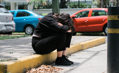 lonely young woman dressed in black sitting on a sidewalk in the street quite sad probably after...